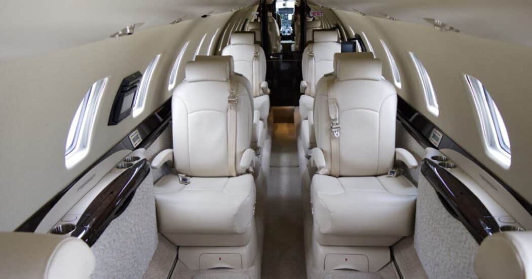 Interior of a luxurious private jet with cream leather reclining seats and wood panel details, arranged in two rows facing each other.