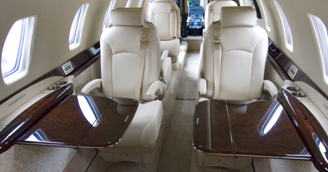 Luxurious private jet interior with cream leather seats and polished wood tables, looking towards the cockpit.