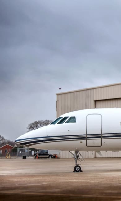 Falcon 2000 EX - 2008 - Mobile - 2 A private jet is parked on a tarmac near a beige hangar under a cloudy sky.