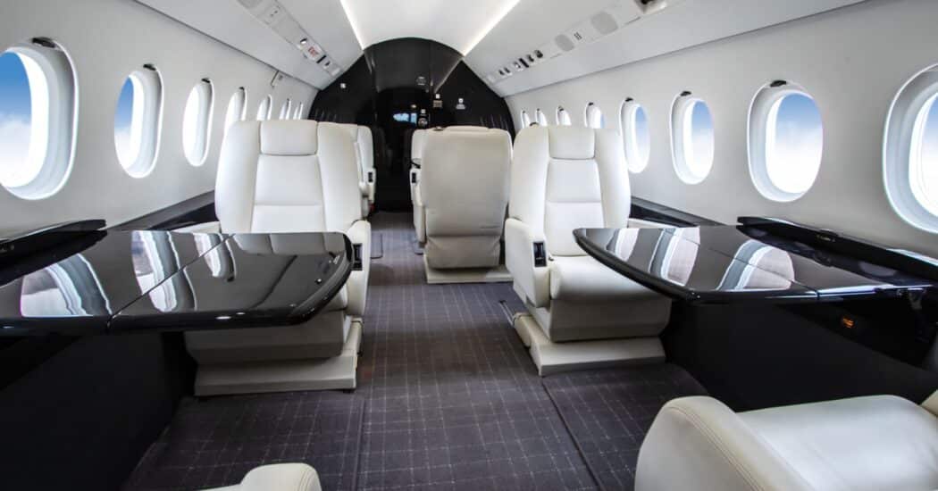 Interior of a private jet with luxurious white leather seats and glossy black tables, featuring multiple oval windows.