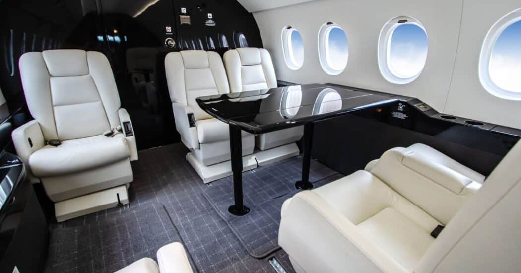 Luxurious private jet interior with white leather seats and a dark glossy table, surrounded by round windows.