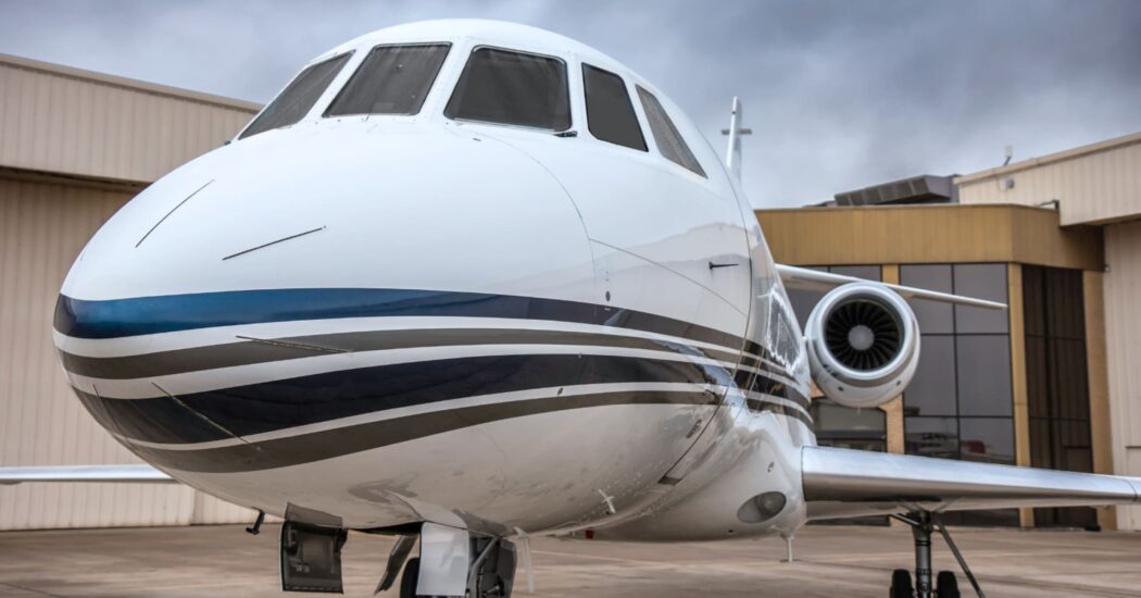 Close-up of a sleek private jet parked in front of a hangar under a cloudy sky.