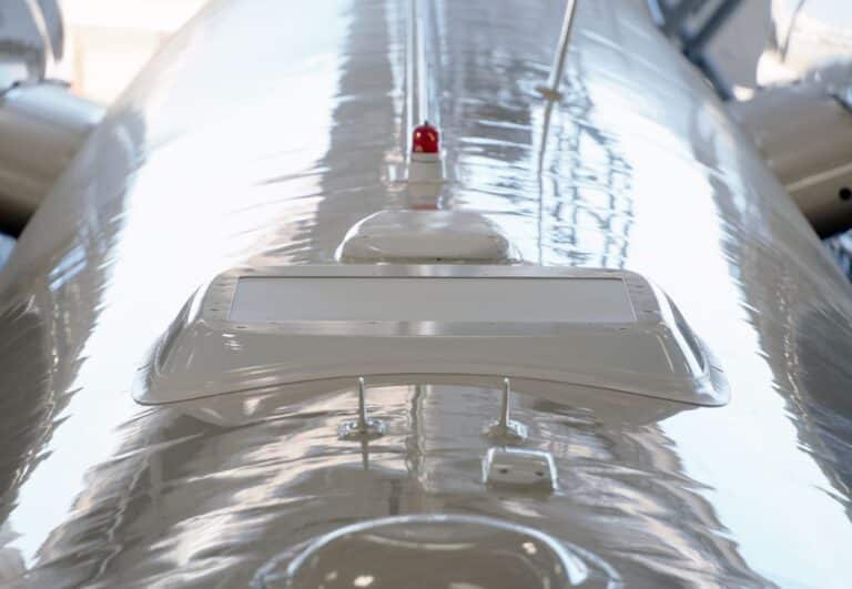 Close-up of a sleek, reflective surface with a red light and various antennas on a modern aircraft fuselage.