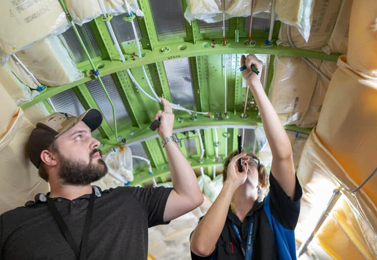 Two maintenance technicians performing work on the interior of an aircraft cabin