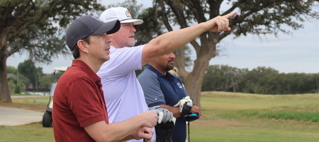Three golfers at the Busines Jet Charity Golf Tournament pointing off into the distance