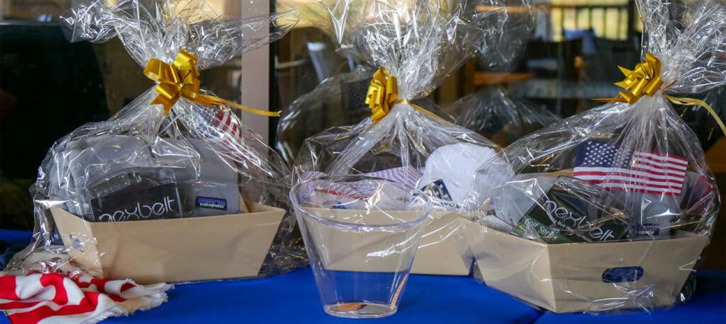 Three raffle prize baskets on a blue table with a clear bucket in front of them