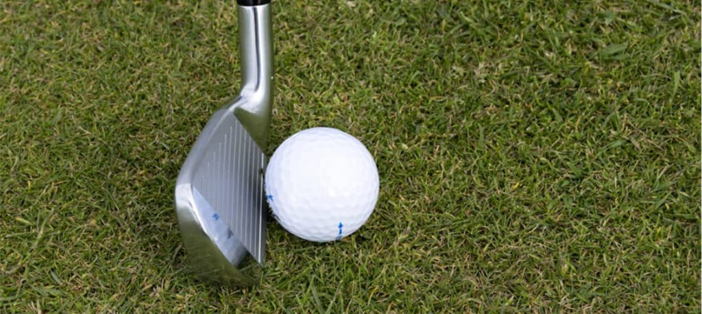 A golf ball with a golf club lined up behind it on the green