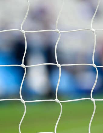 Soccer net against a blurry background of a soccer pitch and a crowd