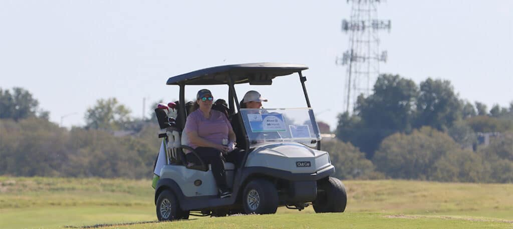 two ladies in a golf cart on a golf green at the Business Jet Cares Charity Golf Tournament