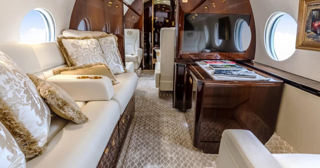 Business jet Charter Gulfstream G550 cabin featuring a four-place divan, TV, and storage space