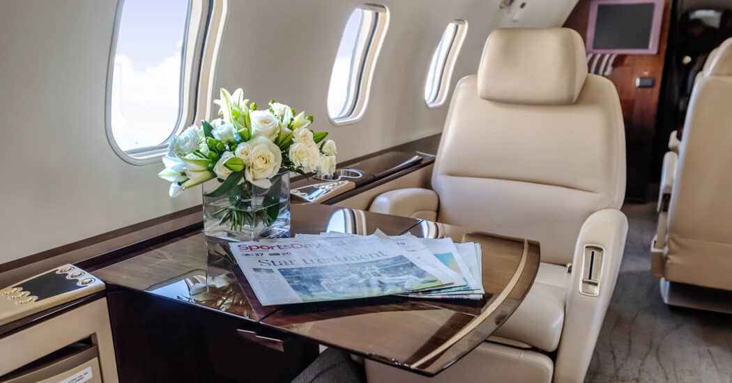 A leather seat on a private jet with a newspaper and flowers on the table
